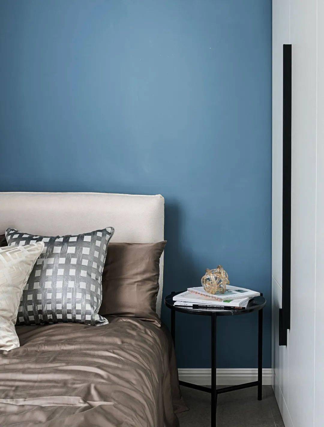 卧室空间在蓝色的床头墙基础,布置米白色布艺床,香槟色的床单,也