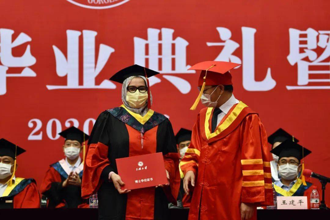 教授为获得学位的毕业生代表颁发学位证书、扶正流苏并与他们合影留念。