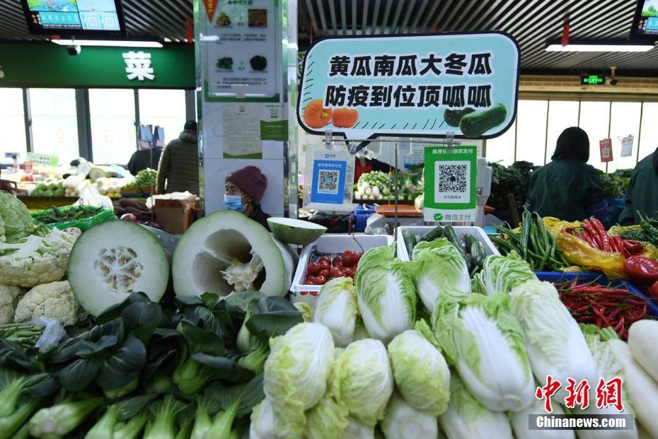 图为一蔬菜摊位上摆放着"黄瓜南瓜大冬瓜,防疫到位顶呱呱"的标语.