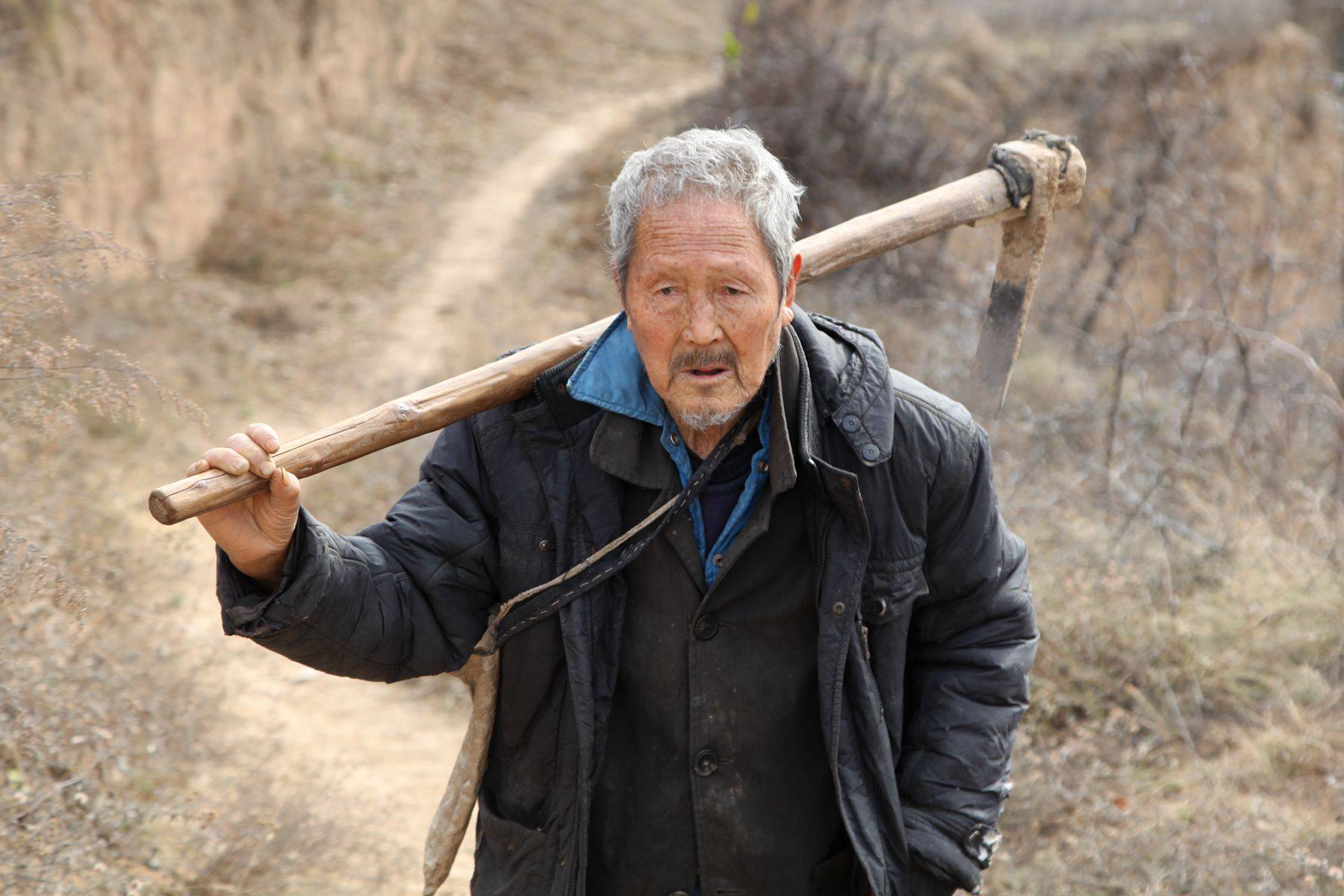 我们在山沟沟里遇到了一位老人家,他扛着䦆头,背着布袋走在下地干活的