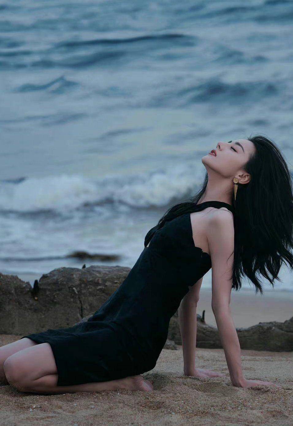 只见迪丽热巴身穿黑色镂空晚礼服赤脚走在沙滩上.