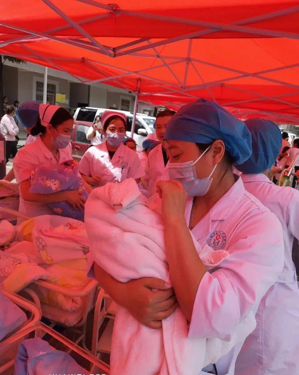 照片,空旷安全的场地上,二十多位穿着白大褂的医生怀里都抱着一个婴儿