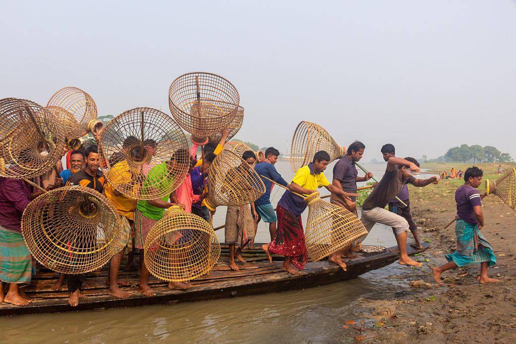 孟加拉渔民手持竹篮参加传统钓鱼节 集体搭船渡河颇为拥挤