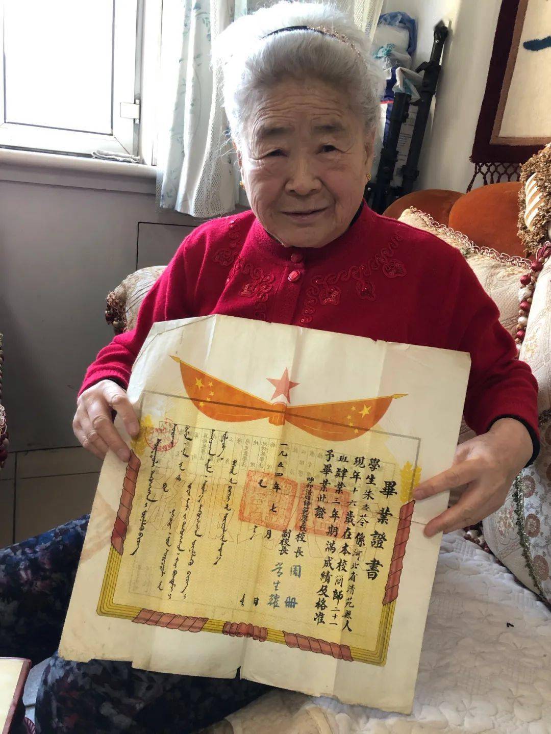 (朱秀玲手持自己1954年师范学校毕业证书)