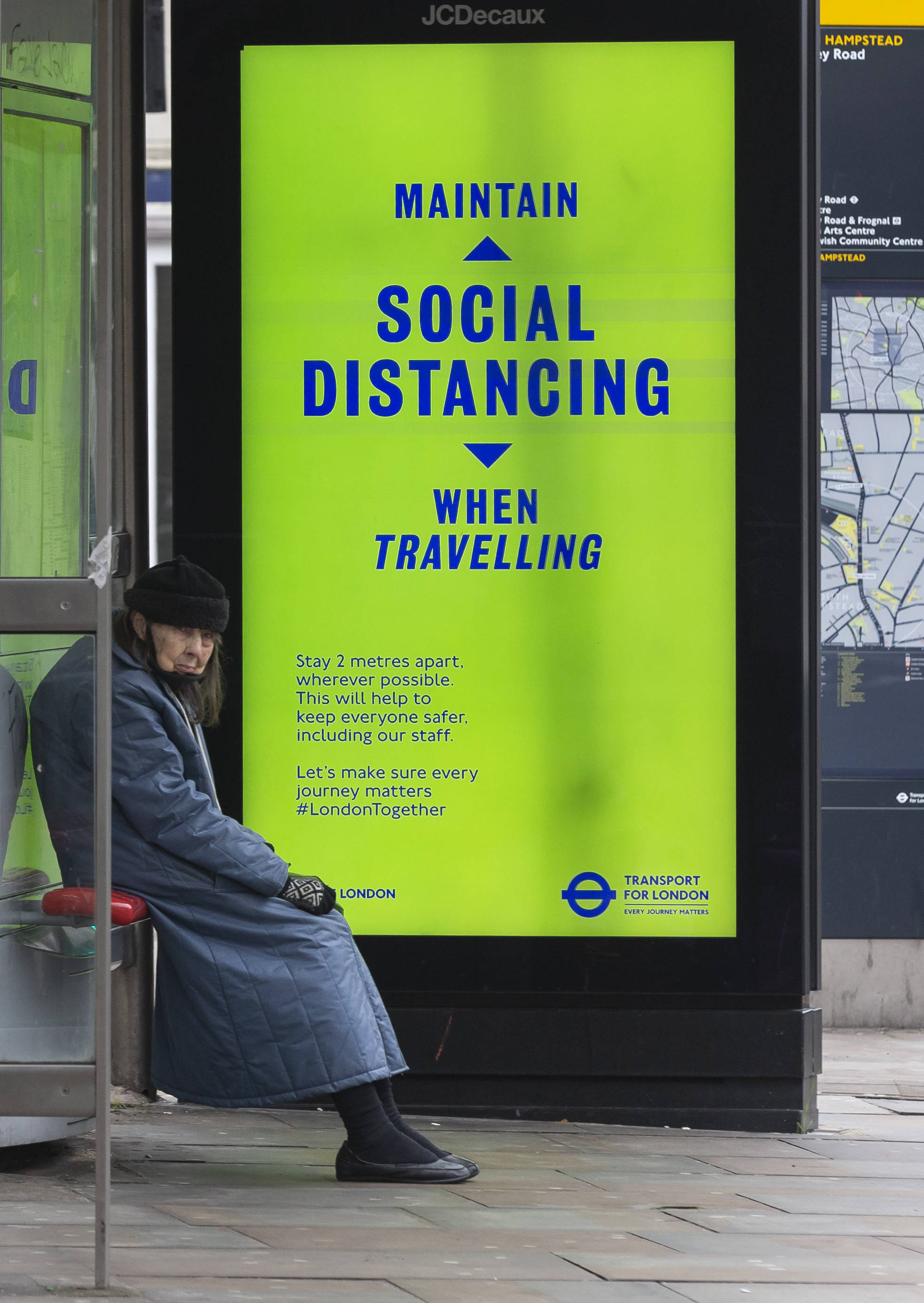 1月10日,一名乘客在英国伦敦一处公交车站等车,广告牌上显示"旅途中请