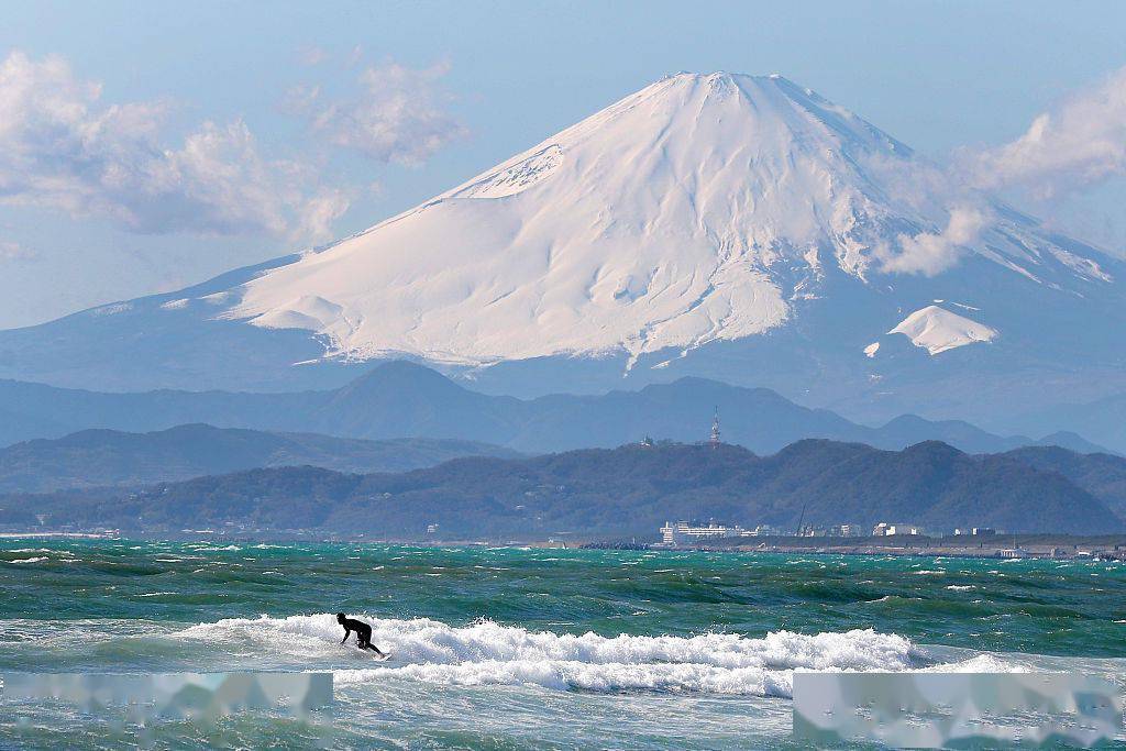 日本东京,男子在江之岛海边冲浪为东京奥运会预热,远处就是富士山.