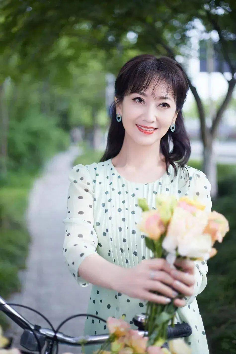 看这张照片里面的赵雅芝,穿着一件绿色的波点裙,手捧着一束花,看起来