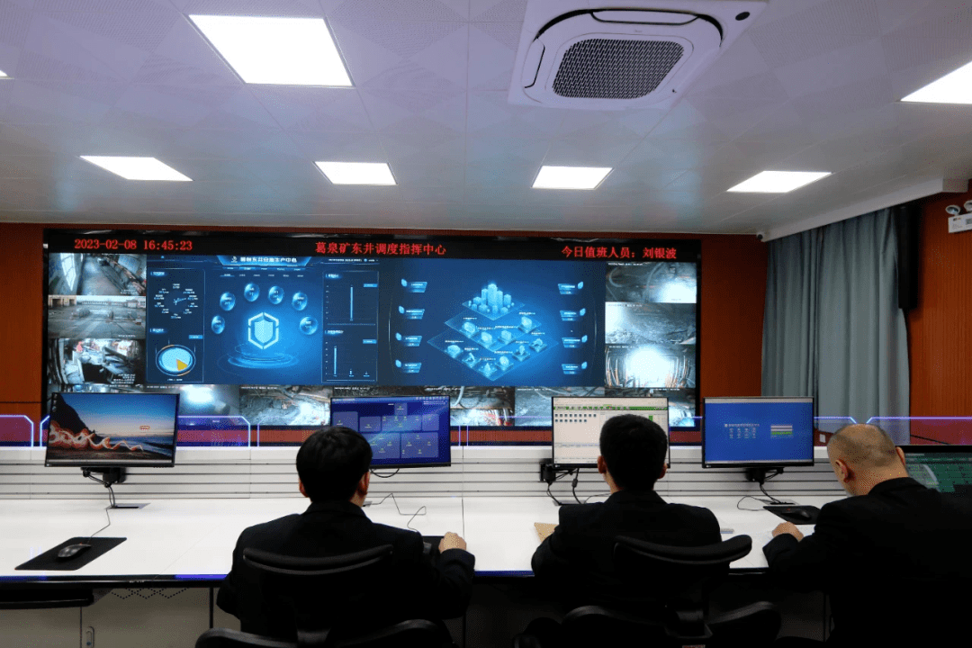 的液晶屏前摆放着一排电脑,操作人员操控监测着各个工作场所,视频监控